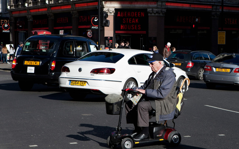 Elderly man drive mobility scooter through the London street.