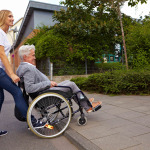 Young woman helping elderly woman in wheelchair over a curbstone