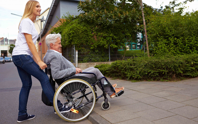 Young woman helping elderly woman in wheelchair over a curbstone