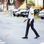 Young African Blind Man Wearing Armband Walking With Stick Crossing Road