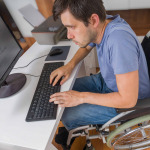 man in wheelchair is working with computer in office.