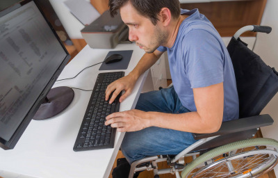 man in wheelchair is working with computer in office.