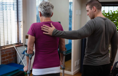 Physiotherapist assisting senior woman patient to walk with crutches
