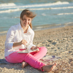 Cute Girl with Down syndrome on the beach play with the tablet.