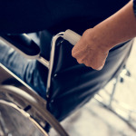 Closeup of person hands pushing the man in wheelchair