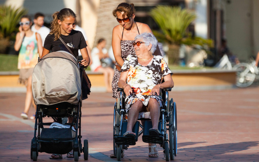 A woman pushing the wheelchair with his mother over.