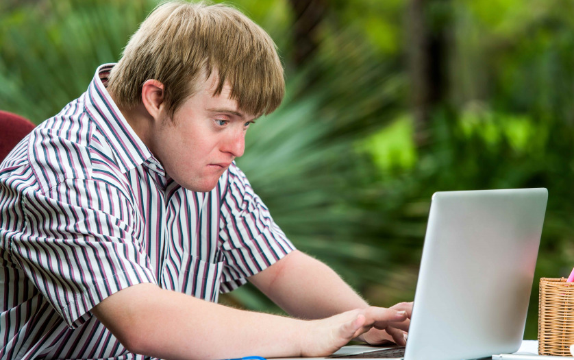 Portrait of concentrated young man with down syndrome working on laptop outdoors.