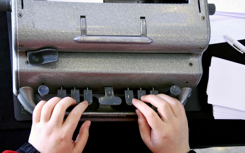Flat lay view of hands of a person typing on a braille typing machine