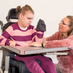 A disabled child in a wheelchair being cared for by a voluntary care worker who is helping with personal hygiene.