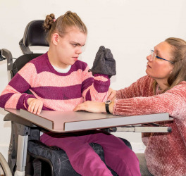 A disabled child in a wheelchair being cared for by a voluntary care worker who is helping with personal hygiene.