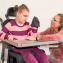 A disabled child in a wheelchair being cared for by a voluntary care worker who is helping with personal hygiene.