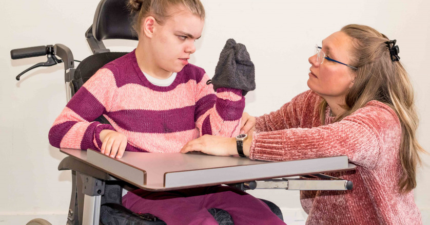 A disabled child in a wheelchair being cared for by a voluntary care worker who is helping with personal hygiene.