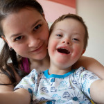 Selfie of cute small boy with Down syndrome with his young mother