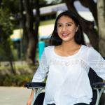 Young brunette woman sitting in wheelchair smiling, outdoors