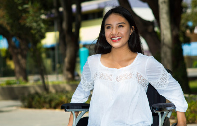 Young brunette woman sitting in wheelchair smiling, outdoors