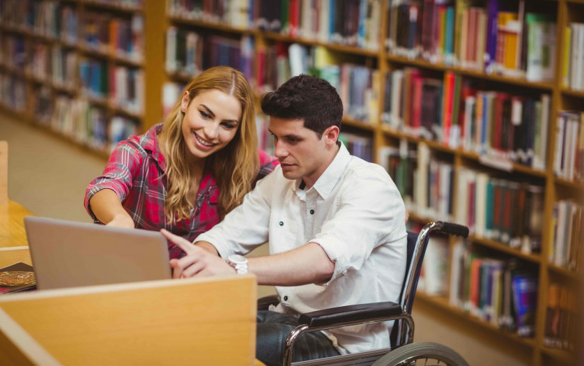 Student in wheelchair working with a classmate in library