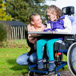 Child in a wheelchair relaxing outside with a care assistant