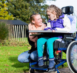 Child in a wheelchair relaxing outside with a care assistant