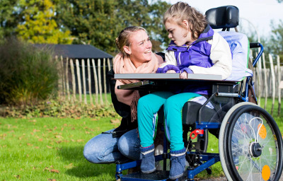Child in a wheelchair relaxing outside with a care assistant