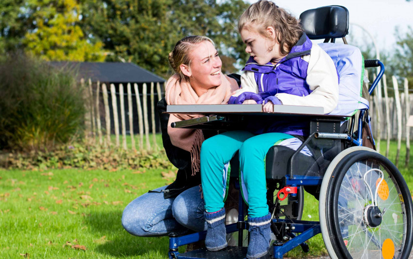 Child in a wheelchair relaxing outside with a care assistant