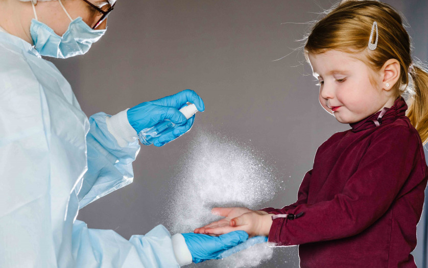 nurse in a protective suit, mask tells child how to use the sanitizer