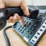 Male hand holding telephone receiver while dialing a telephone number to make a call