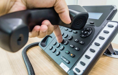 Male hand holding telephone receiver while dialing a telephone number to make a call