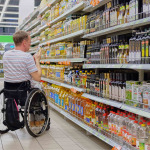 a man in a wheelchair selects goods on store shelves and makes purchases in a supermarket