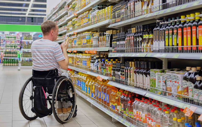 a man in a wheelchair selects goods on store shelves and makes purchases in a supermarket