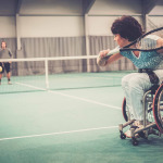 woman on wheelchair playing tennis on tennis court.