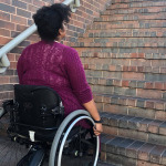 A young African American woman in a wheelchair looking up a flight of stairs
