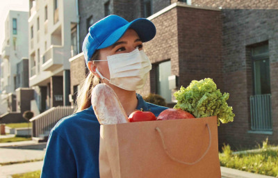 Close up portrait young courier woman holding food craft bag. Modern safety food delivery service. A delivery woman wearing medical mask.