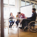 Coworker on wheelchair with photo editors in meeting room