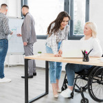 Side view of woman in wheelchair conversing with female coworker at the office