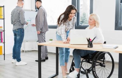 Side view of woman in wheelchair conversing with female coworker at the office