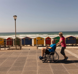 Side view of disabled man being pushed on wheelchair by senior woman at beach on a sunny day