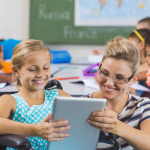 Schoolgirl in wheelchair and teacher using digital tablet in classroom