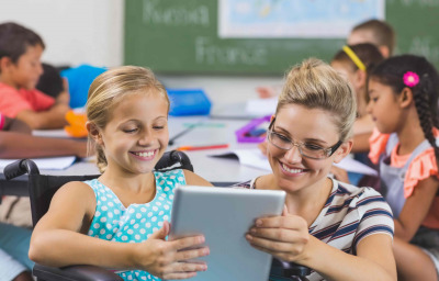 Schoolgirl in wheelchair and teacher using digital tablet in classroom