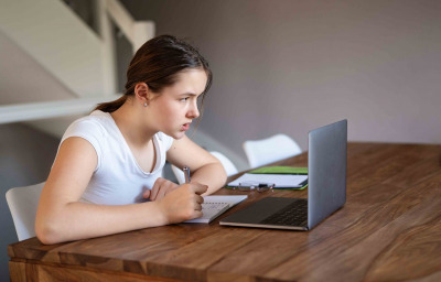 Teenager girl studying online at home looking at laptop
