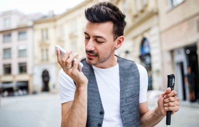 Young blind man with smartphone on street in city, making phone call