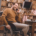 man in wheelchair talking on smartphone and using laptop