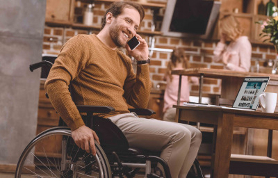 man in wheelchair talking on smartphone and using laptop
