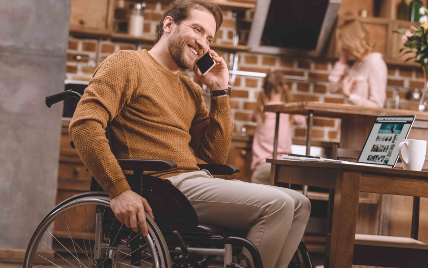 man in wheelchair talking on smartphone and using laptop