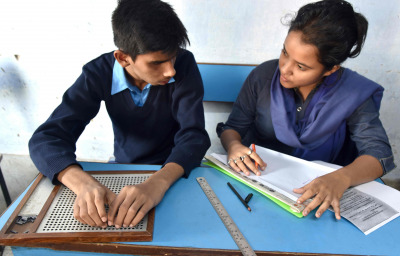 A blind Indian student giving examination to the teacher in a class room