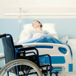 Hospitalized patient lying in bed and wheelchair in the foreground