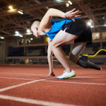 Young man with artificial leg leaning over race track while standing by start line and waiting for signal to go
