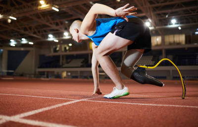 Young man with artificial leg leaning over race track while standing by start line and waiting for signal to go