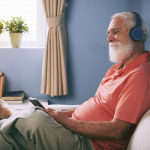 Side view of smiling senior man watching movie on tablet pc at home using wireless headphones