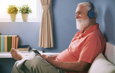 Side view of smiling senior man watching movie on tablet pc at home using wireless headphones