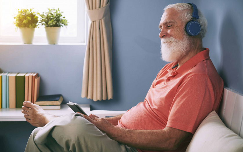 Side view of smiling senior man watching movie on tablet pc at home using wireless headphones
